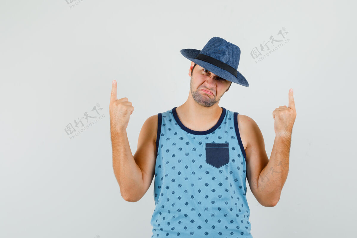 手指一个穿着蓝色单品的年轻人 戴着帽子 手指朝上 看上去很不高兴 胡茬发型单身