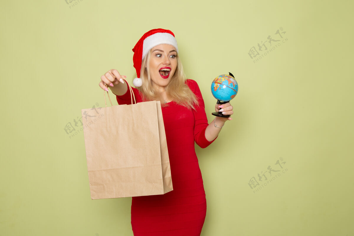 颜色正面图美女手持小地球仪和包裹在绿色墙上的彩雪节日圣诞新年感慨圣诞节喜剧演员小