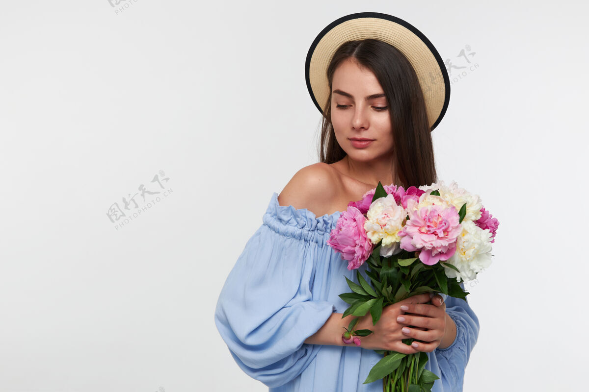 模特十几岁的女孩 快乐的女人 深色长发 戴着帽子 穿着蓝色的裙子 手里拿着一束漂亮的花 在白墙上的复印区左下角看着面部头发姿势