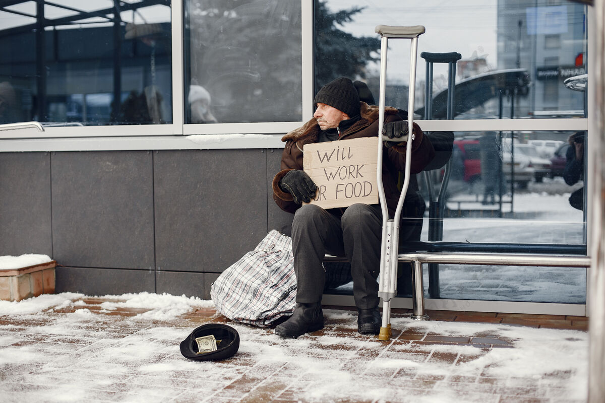 孤独无家可归的人坐在大楼附近人手帽子