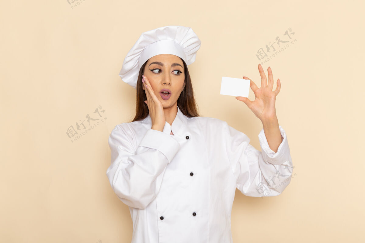 举行身穿白色厨师服的年轻女厨师手持白色卡片在浅白的桌子上的正面视图烹饪厨房工作烹饪工人肖像工人烹饪