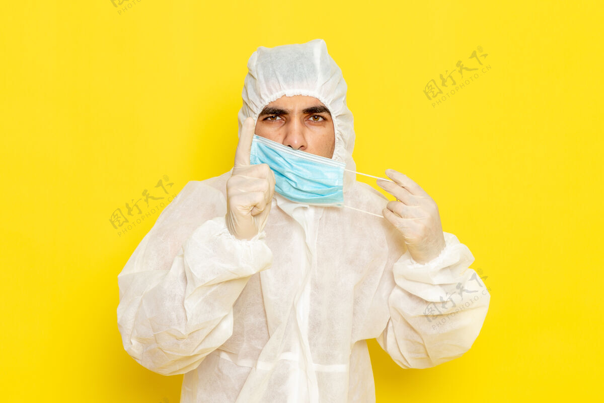 防护身穿特殊防护服的男科学工作者在黄色墙壁上脱下面具的正面图带特殊面罩