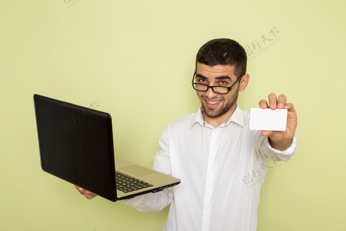 实验室身穿白衬衫 手持白卡和笔记本电脑的男上班族在绿色墙上的正视图电脑工作前面