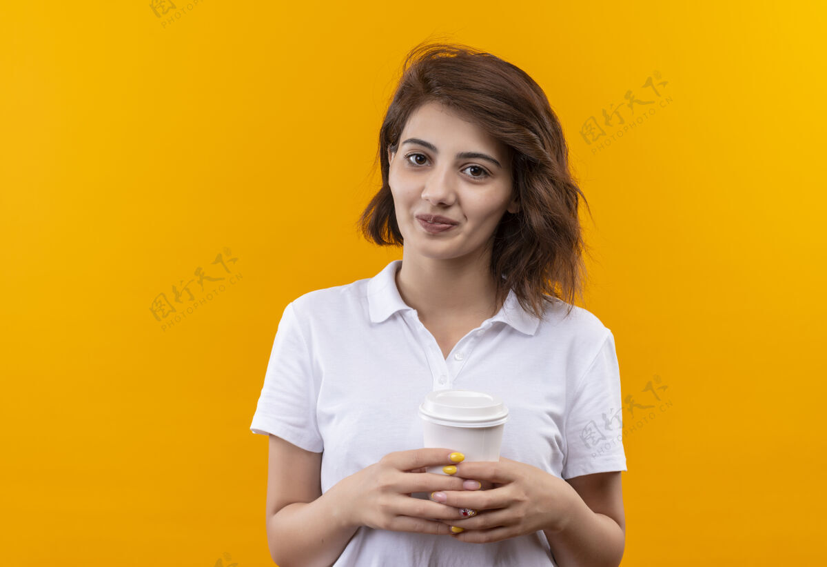 年轻一个留着短发的小女孩 穿着白色马球衫 手里拿着咖啡杯 看着镜头 满脸笑容快乐穿女孩