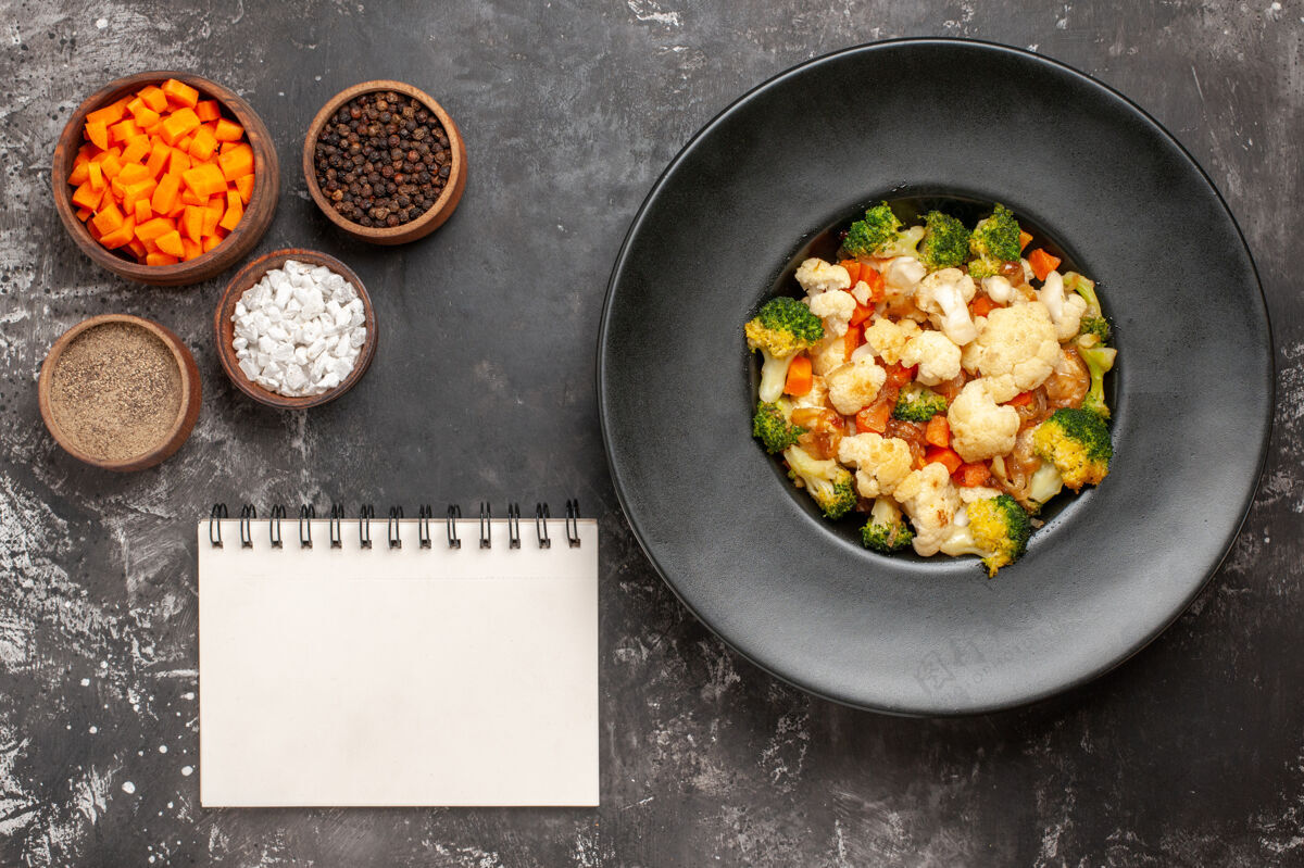 沙拉俯视图西兰花和花椰菜沙拉在黑碗不同的香料和削减胡萝卜碗笔记本在黑暗的表面炒锅胡萝卜视图
