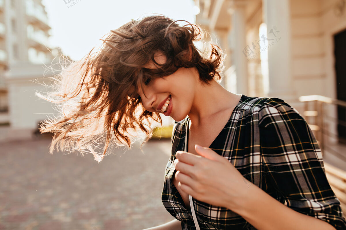 户外放松的白人女孩在街上挥舞着她的头发在秋天的日子里 穿着格子衬衫 站在户外微笑的快乐女人肖像漂亮卷曲