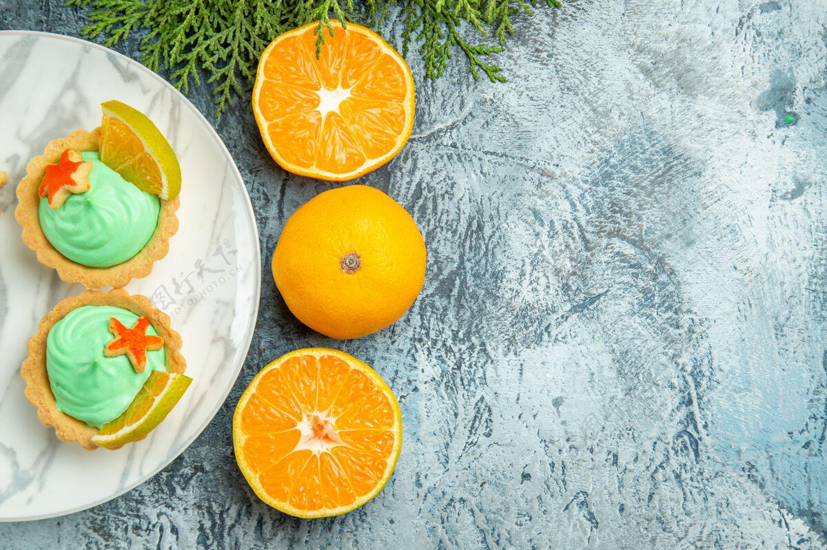 酸的顶视图小馅饼与绿色糕点奶油和柠檬片在盘子上切橘子在黑暗的桌子上复制空间小的盘子甜味