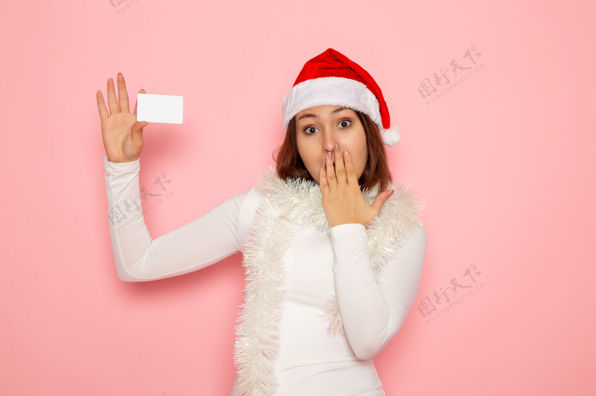 风景正面图年轻女性手持白色银行卡在粉色墙上圣诞彩绘节日新年时尚圣诞银行幸福