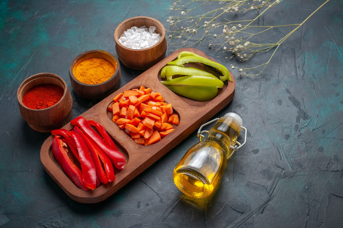 前面前视图切碎的甜椒和调味品 橄榄油在深蓝色的表面蔬菜热的香料