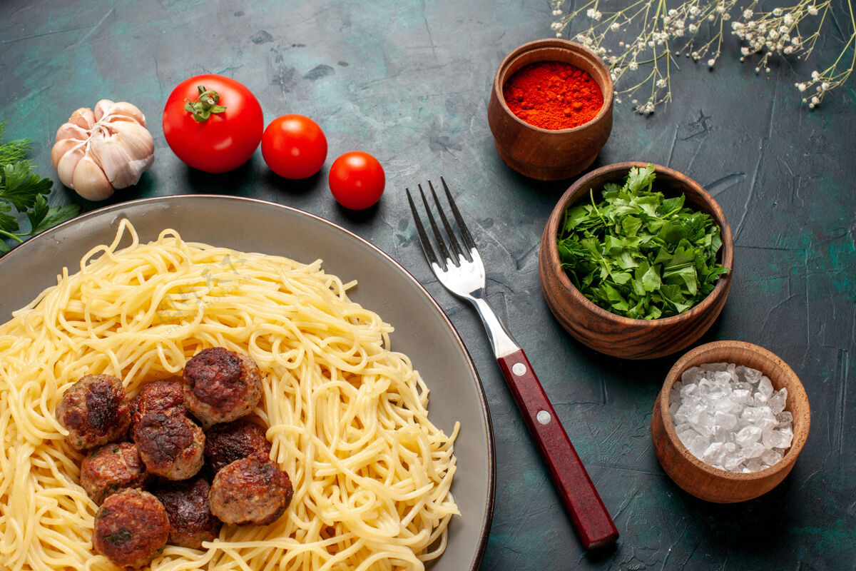 晚餐俯视图煮熟的意大利面食与肉丸调味料和绿色的深蓝色表面熟的肉食品