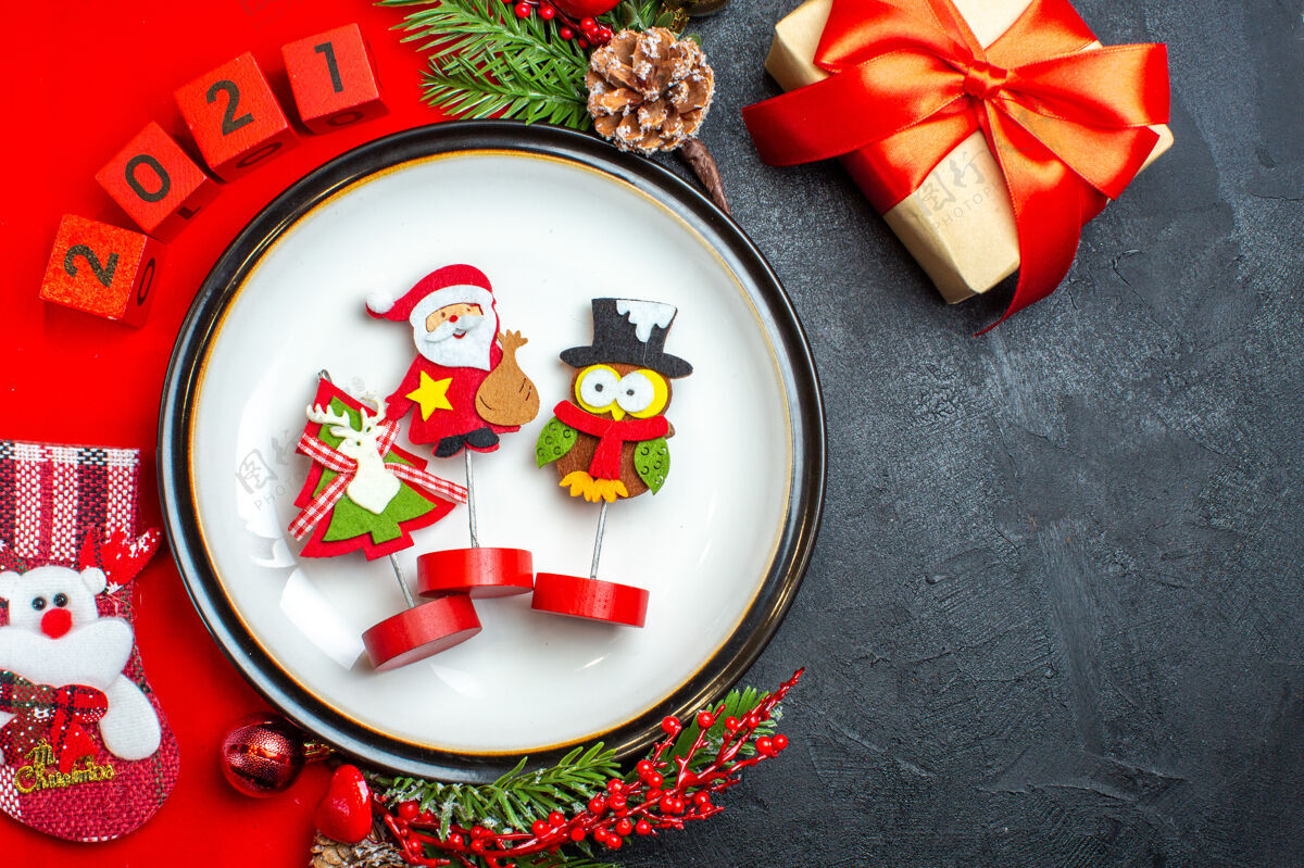 盘子上图为餐盘装饰配件杉木树枝和数字圣诞袜放在一张红色餐巾旁边的一张黑色桌子上的礼物晚餐风景袜子