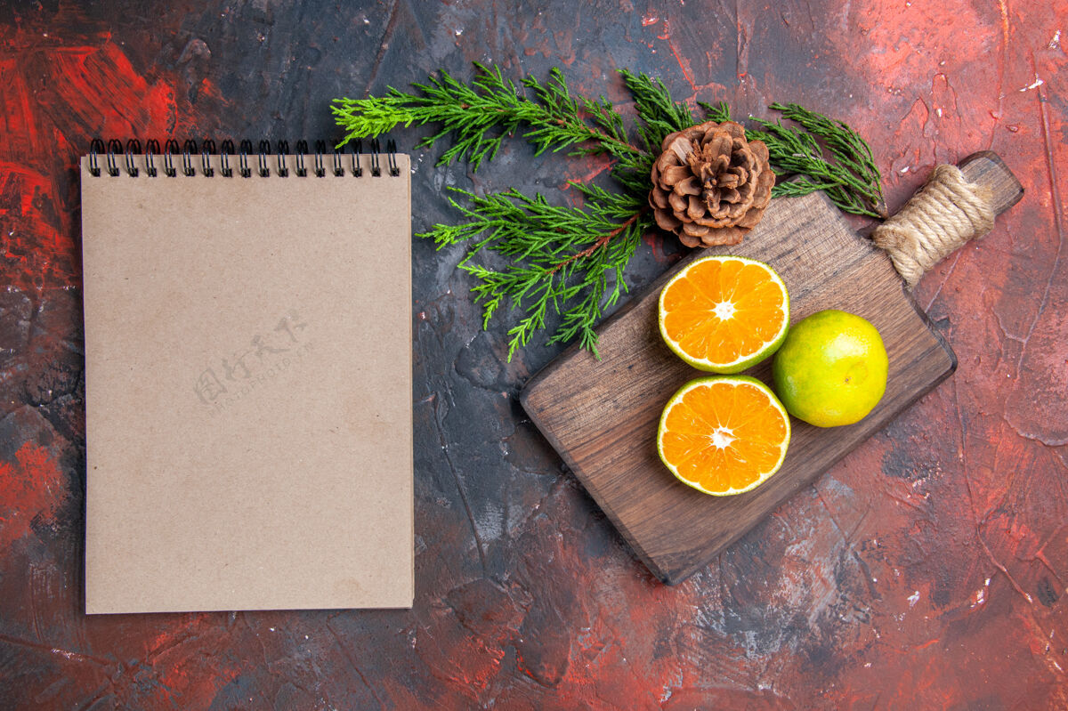 香草俯视图在砧板上切橘子松枝圆锥形笔记本在暗红色的表面视图板子柑橘