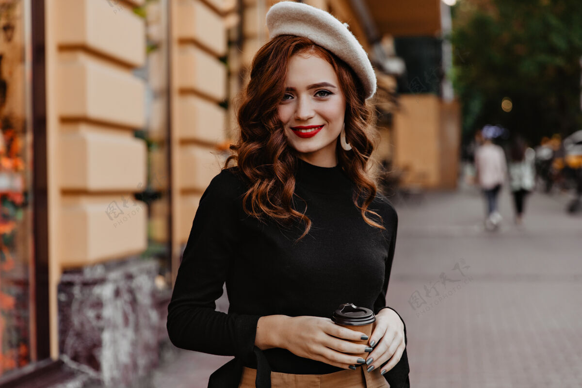 成人害羞的法国女人留着长发在户外摆姿势可爱的红发女士端着咖啡站在街上姜时尚微笑