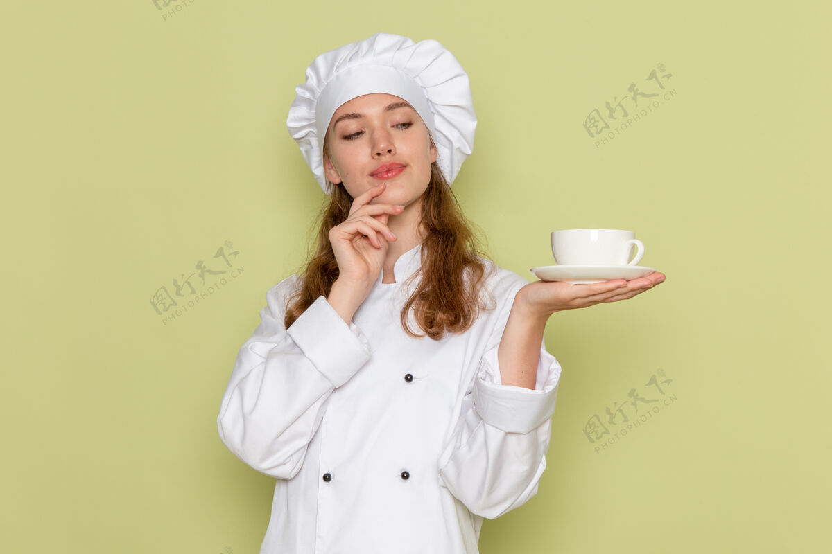 女厨师身着白色厨师服的女厨师正拿着一杯咖啡站在绿色的墙上厨房人杯子