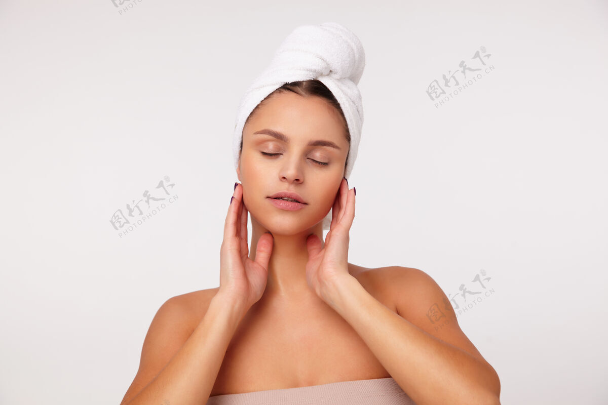 洗澡年轻漂亮的黑发女性闭上眼睛 抬起双手轻轻地触摸脸部 站在白色背景上做美容程序包裹女士女性