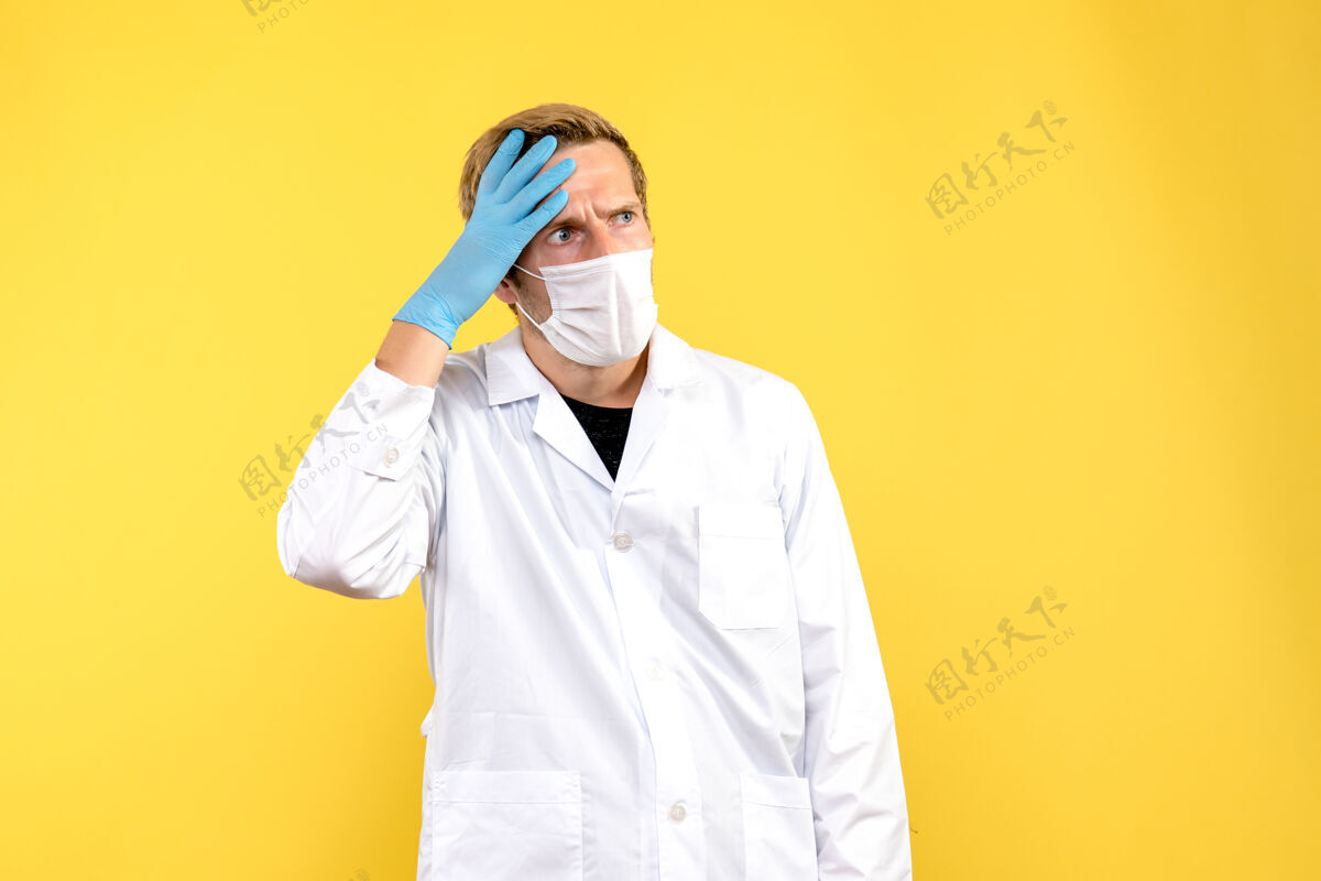 实验室正面图男性医生困惑于黄色背景上的面罩-医疗卫生大流行服装专业人
