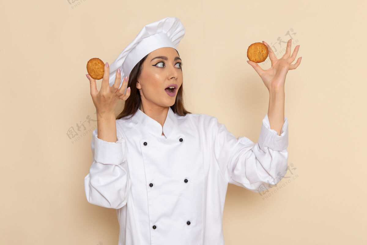 人身穿白色厨师服的年轻女厨师的正面图 在白色的桌子上拿着饼干 在厨房做饭烹饪人食物