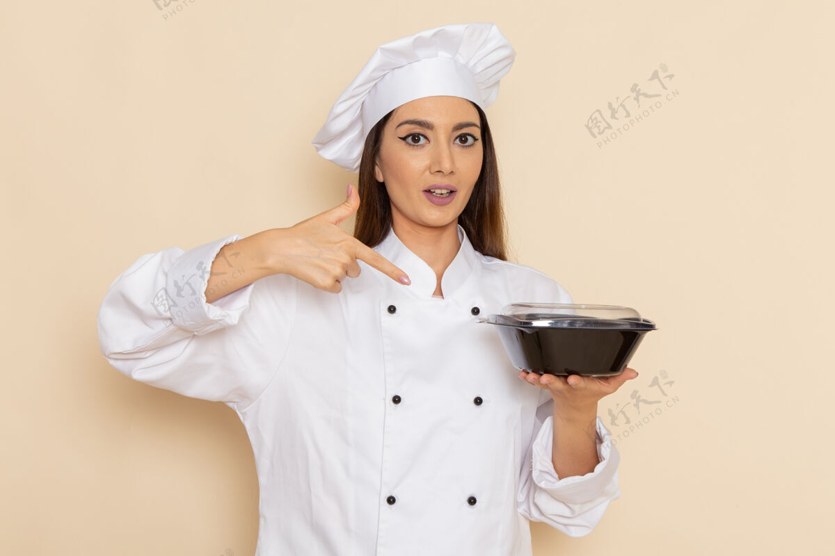 年轻身穿白色厨师服的年轻女厨师正拿着黑碗站在白墙上人护士烹饪
