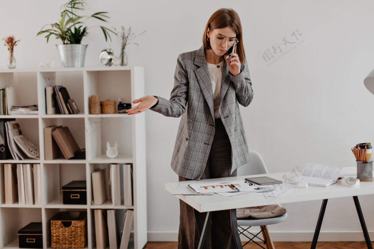 通信穿灰色西装的女人在和商业伙伴通电话看图表的成年女士的肖像办公桌办公室工作