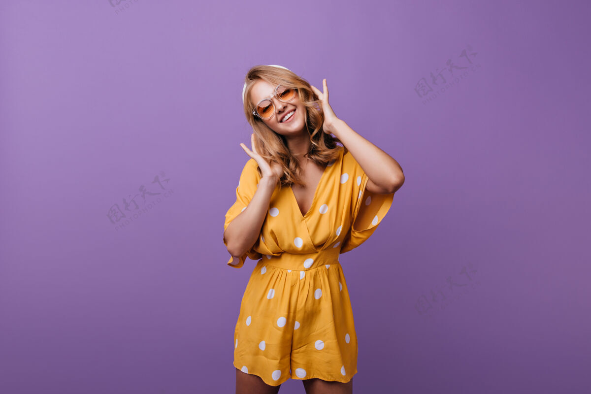 情感开朗匀称的女孩摆出真诚的微笑在紫色的舞台上身着时尚橙色连衣裙的华丽女模特站着模特优雅舞蹈