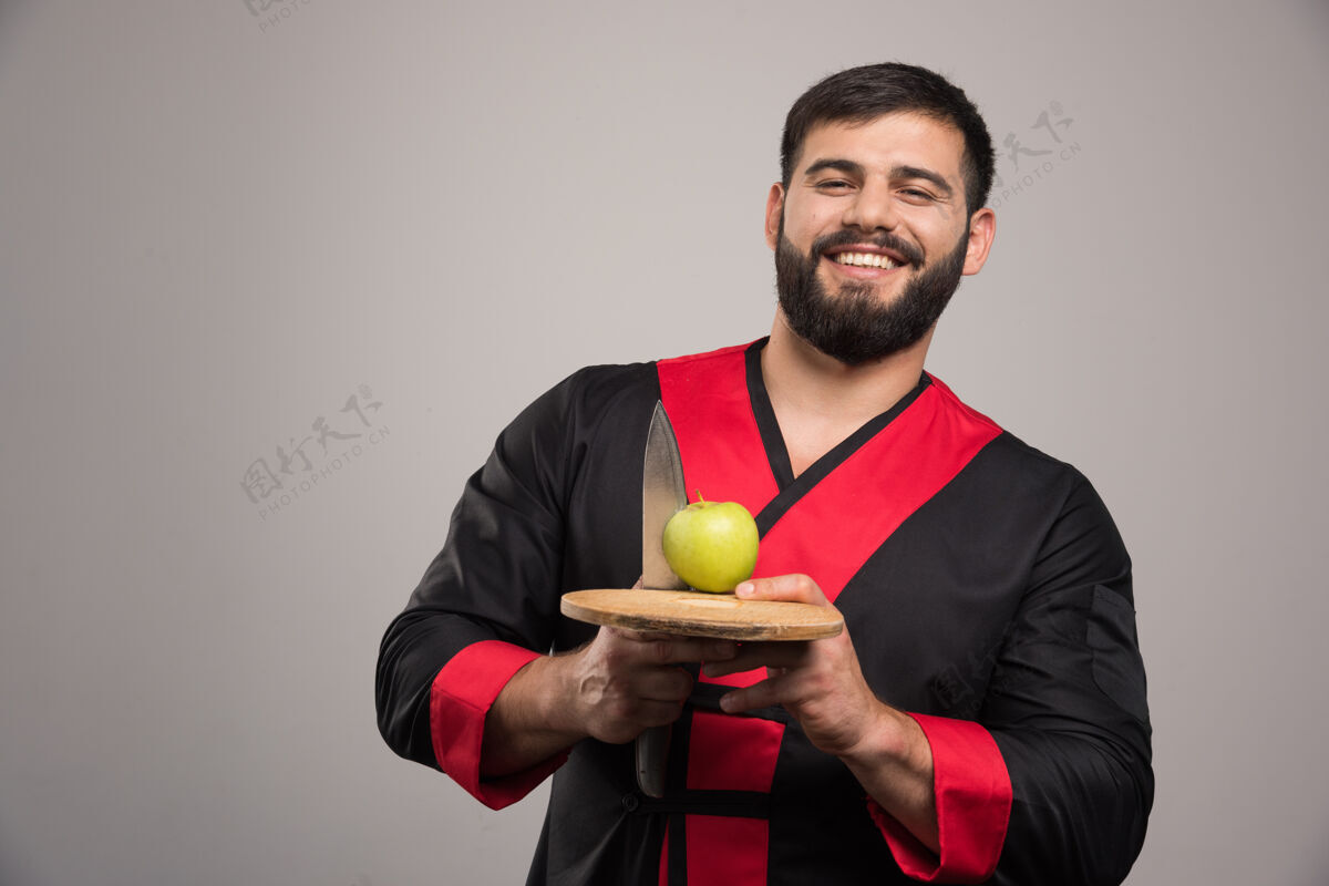 木头微笑的男人拿着一个苹果 刀放在木板上家伙苹果锋利