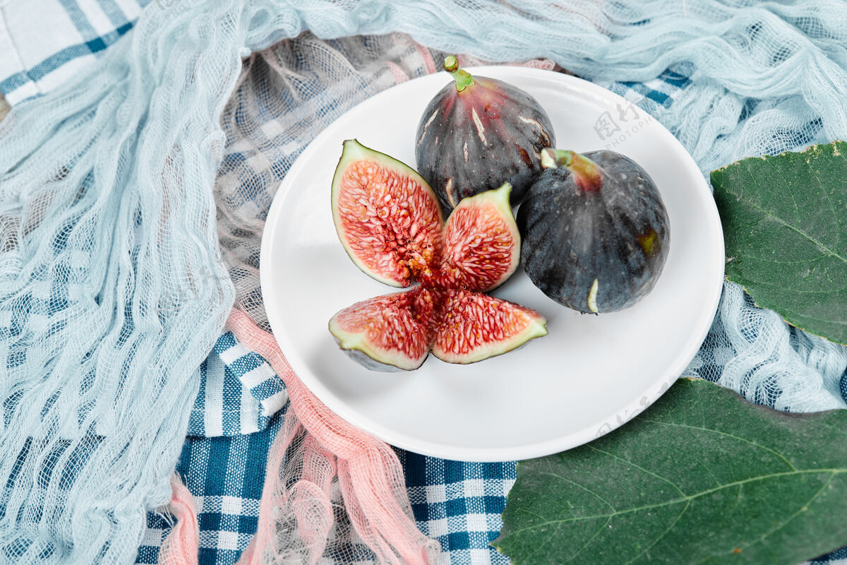 水果一盘完整的 切成薄片的黑色无花果 配上蓝色和粉色的桌布美味新鲜异国情调