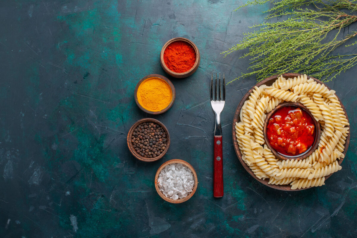 意大利酱在深蓝色的桌子上俯瞰着意大利面食 上面有番茄酱和调味品菜水果盘子