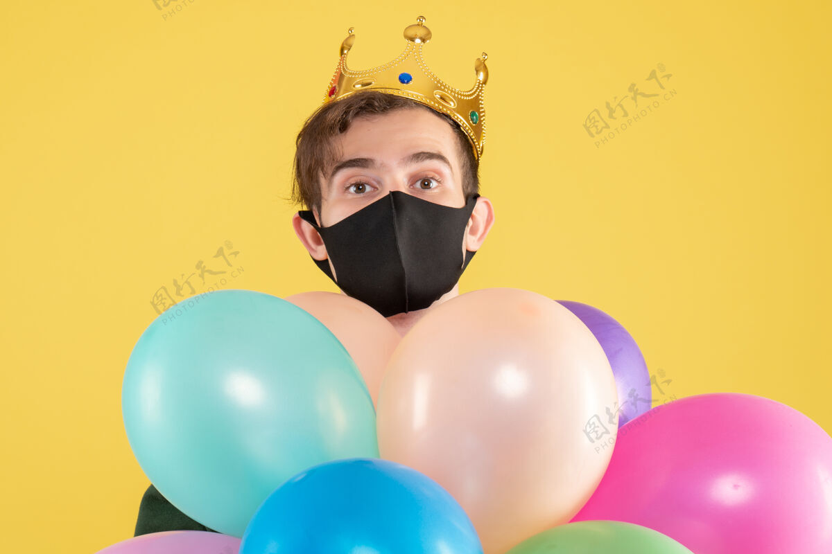 年轻人正面图戴着皇冠和黑色面具的年轻人拿着黄色的气球聚会节日庆祝