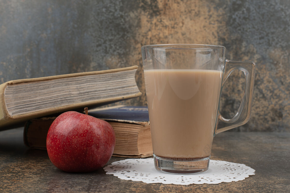 新鲜的一杯热咖啡 一个红苹果和大理石墙上的书玻璃杯饮料大理石