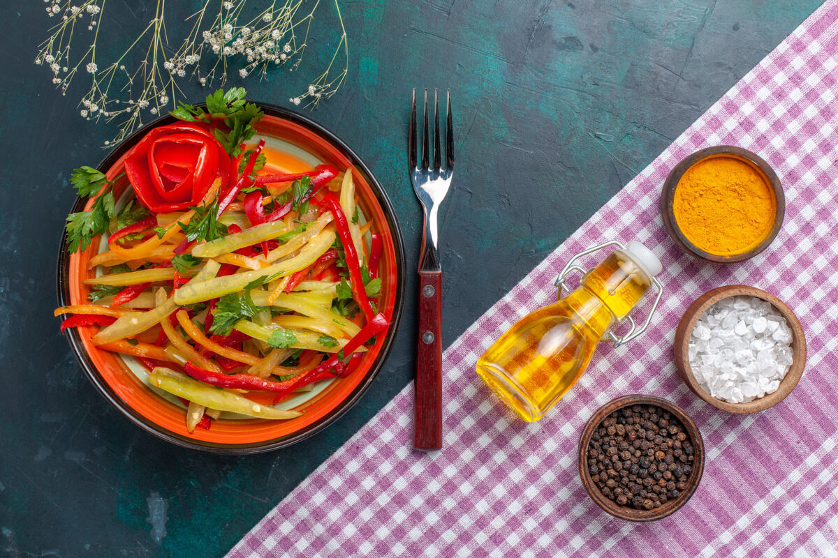 盘子在深蓝色的桌子上俯瞰着切好的甜椒色拉和调味品辛辣辣椒食物