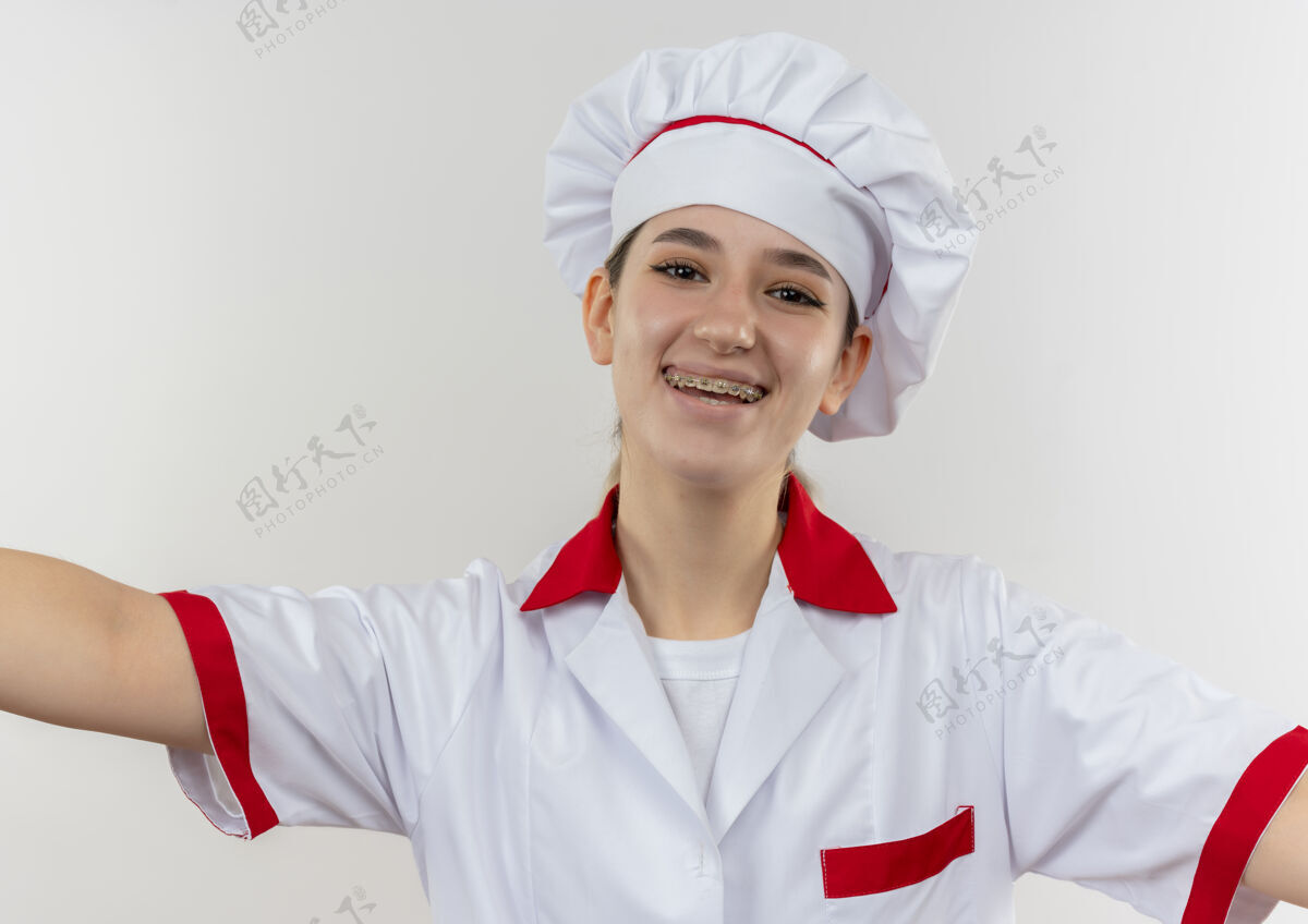 厨师快乐的年轻漂亮厨师穿着厨师制服 戴着牙套 张开双臂孤立在空白处制服手臂年轻