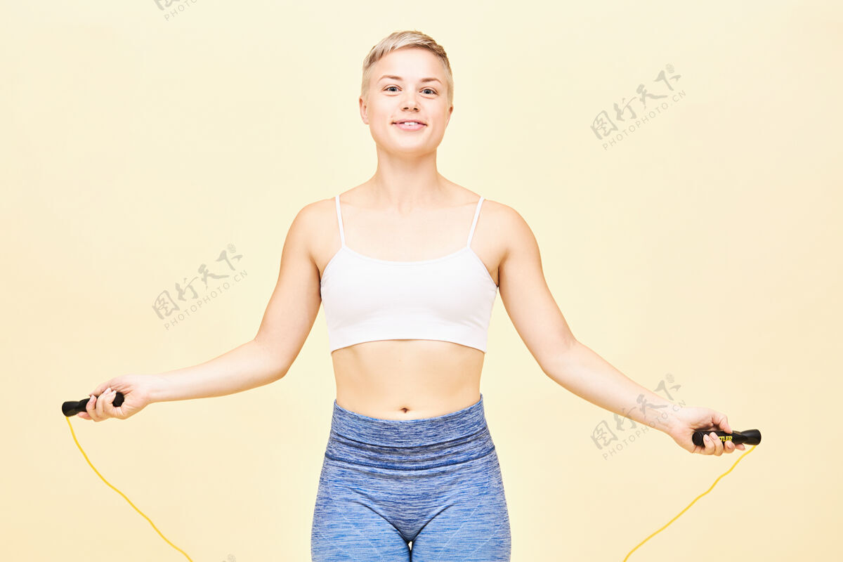 运动身体健康的漂亮精力充沛的女孩 用健身器材燃烧卡路里 跳绳隔离跳跃 做基本的跳跃 有兴奋快乐的表情苗条跳绳绳索