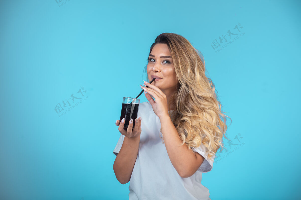 聪明穿着白衬衫的年轻女孩拿着一杯黑鸡尾酒 检查着味道女性女人提神