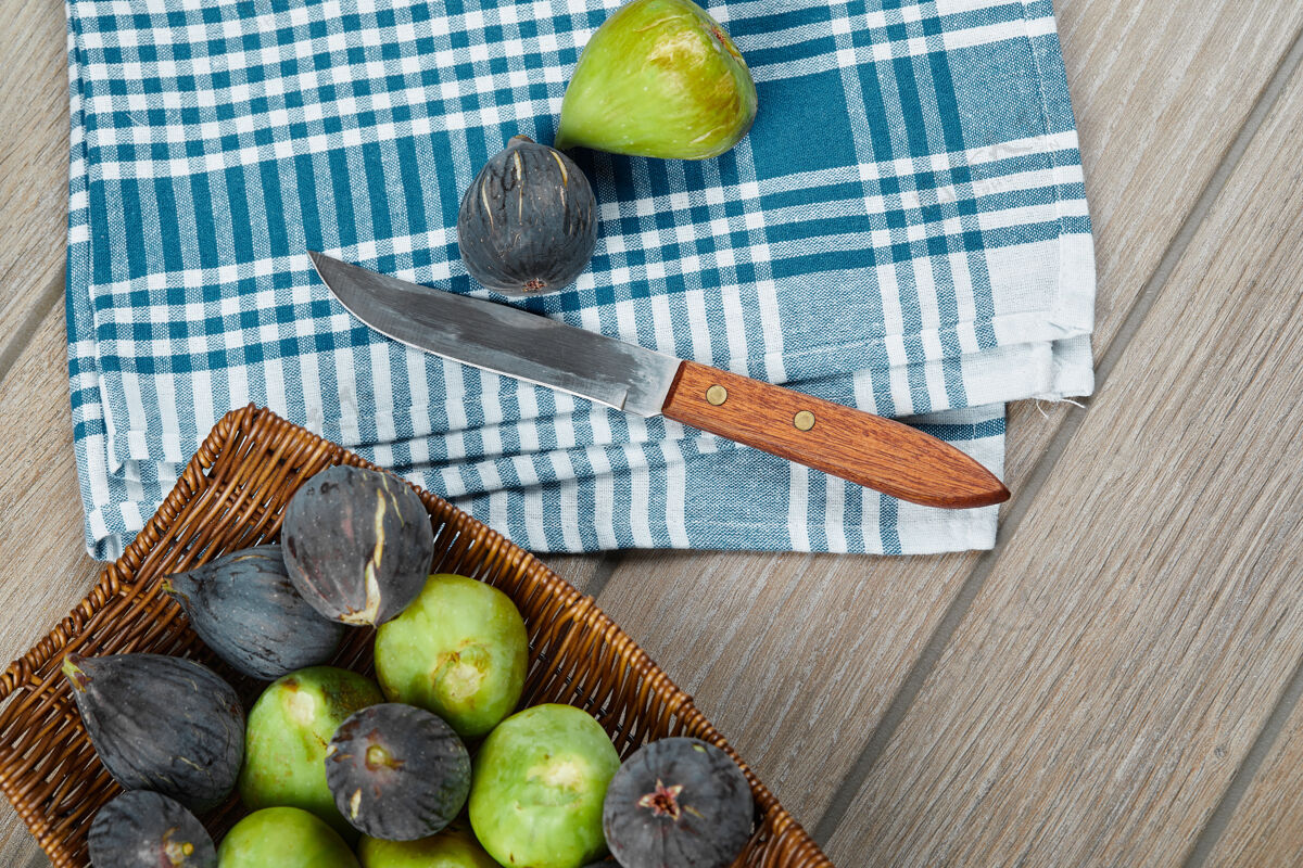 生的木桌上放着一篮子熟无花果 还有一把刀和一块桌布刀食物水果