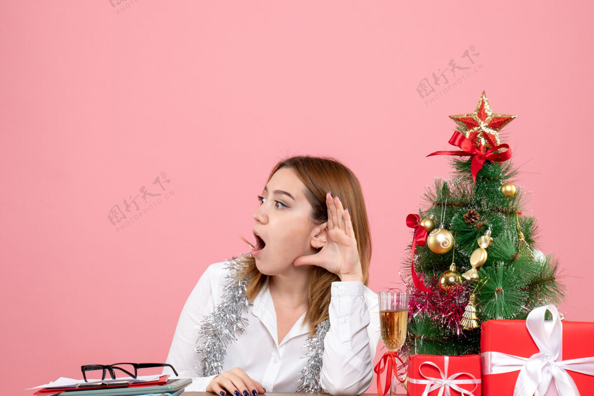 工作女员工坐在桌子后面 手里拿着圣诞礼物 听着粉色的音乐肖像桌子女工人