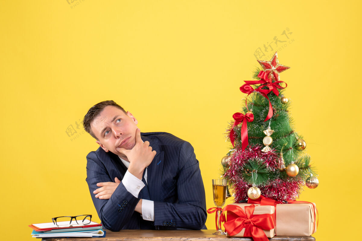 体贴的男人前视图：体贴的男人坐在圣诞树旁的桌子上 黄色的礼物商人坐着西装