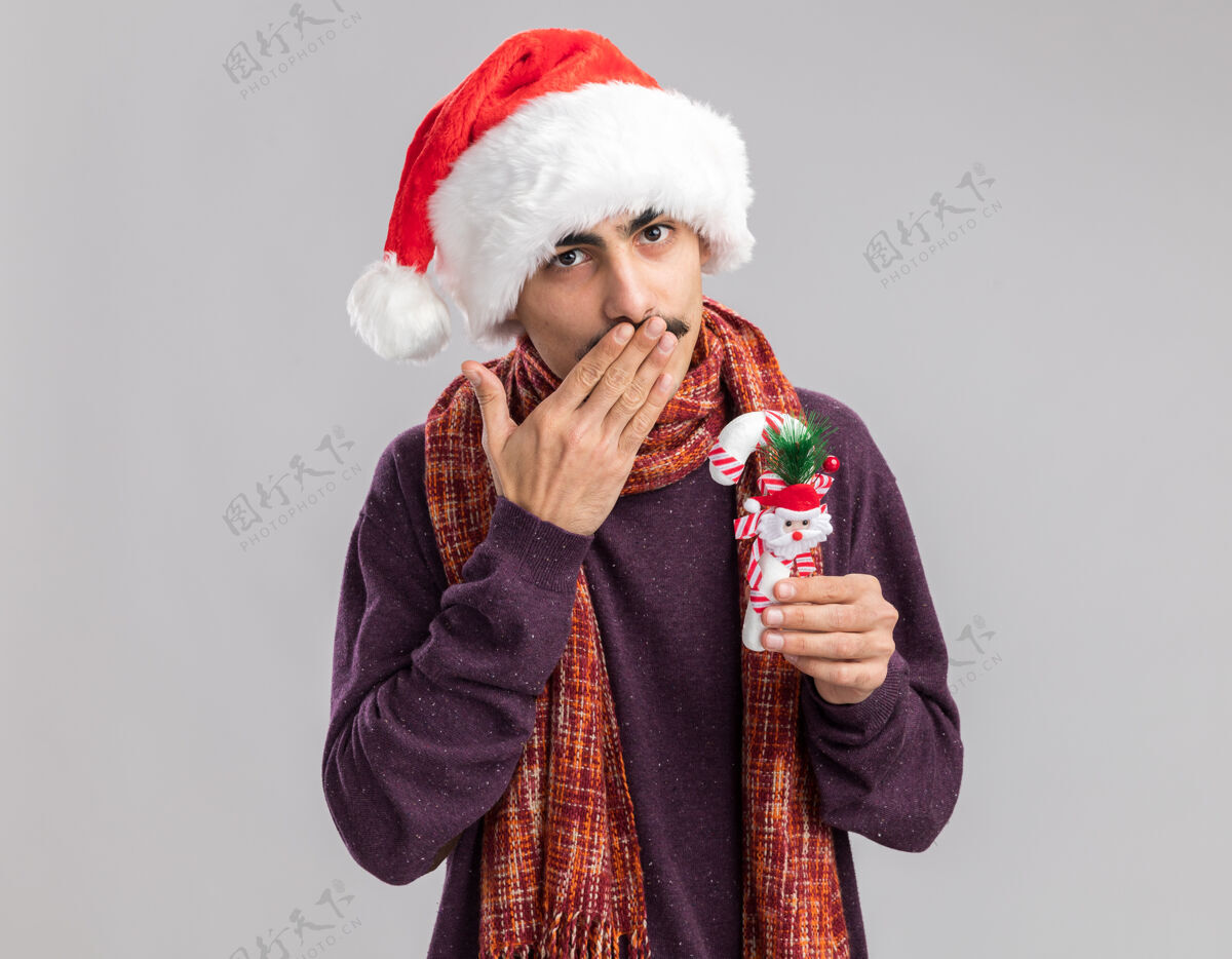 年快乐的小胡子男人戴着圣诞老人的帽子 脖子上围着暖和的围巾 手里拿着圣诞糖果手杖吹着吻男人吻圣诞快乐