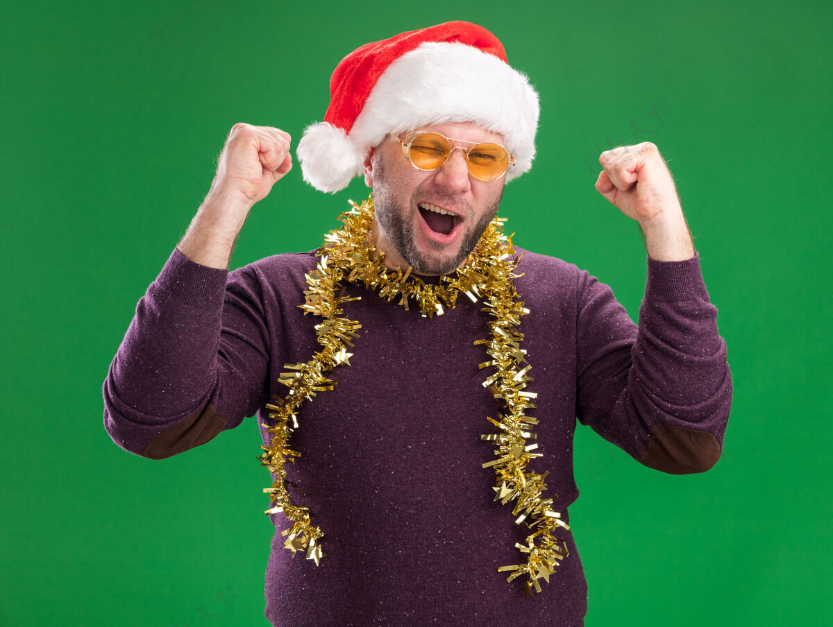 帽子快乐的中年男子戴着圣诞帽 脖子上戴着金箔花环 戴着眼镜 看着相机眨眼 做着“是”的手势 在绿色背景下孤立着金属片脖子男人