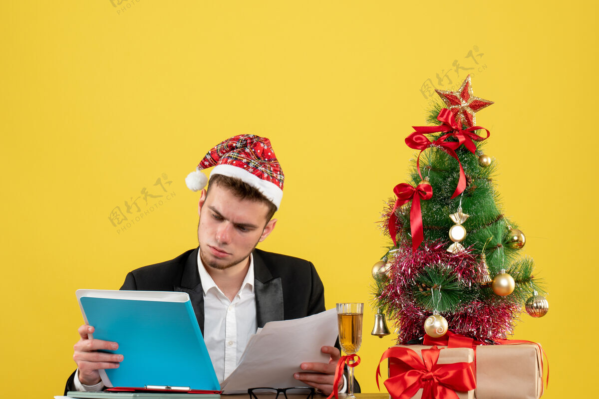 周围前视图男性工人阅读文件周围的小圣诞树和黄色的礼物阅读树年