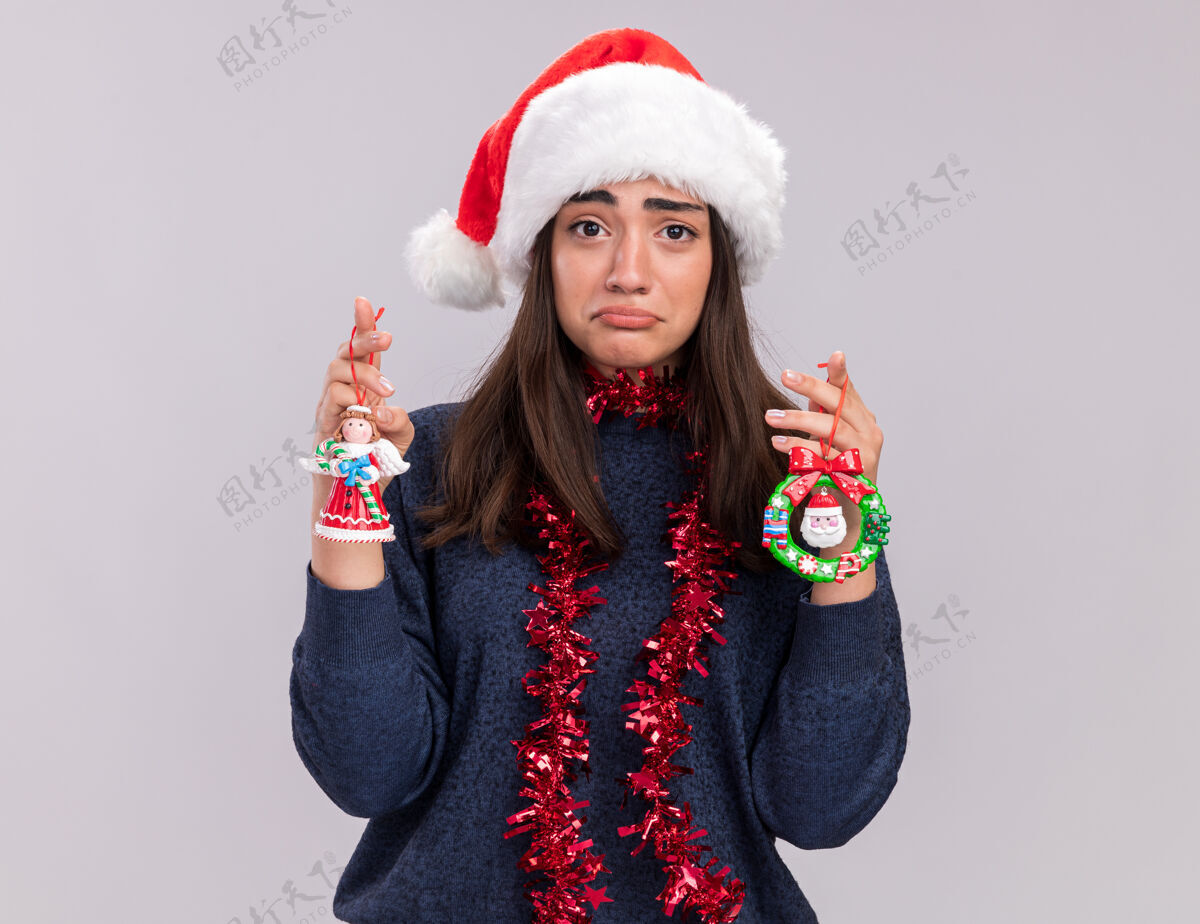 脖子戴着圣诞帽 脖子上戴着花环的白人女孩手里拿着圣诞树玩具悲伤快乐花环