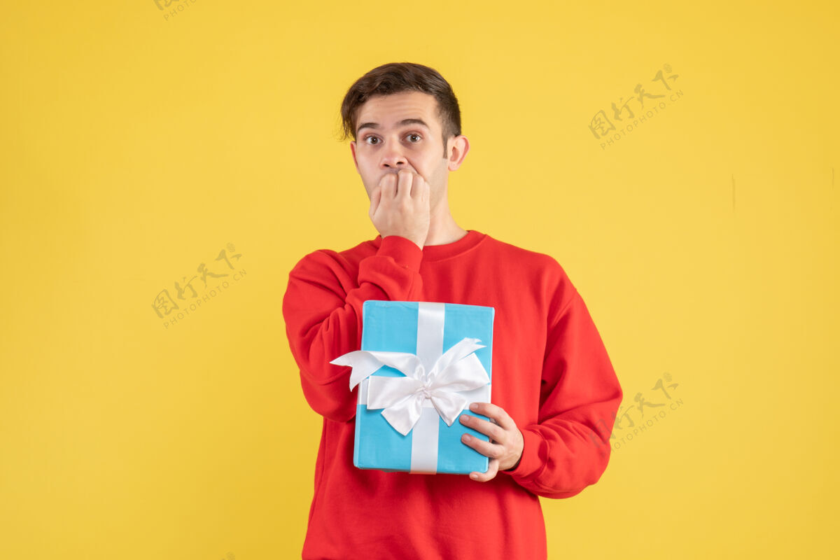 肖像正面图：拿着蓝色礼品盒的年轻人站在黄色的地板上男人脸专业