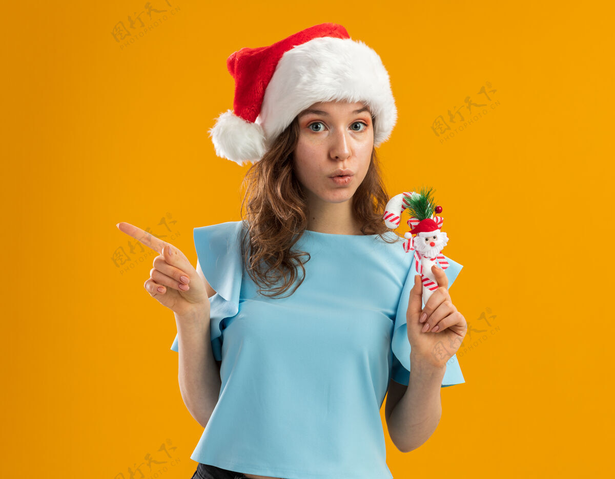 新的身穿蓝色上衣 戴圣诞帽 手持圣诞糖果手杖的年轻女子 用食指指着一旁 神情忧心忡忡女人糖果蓝色