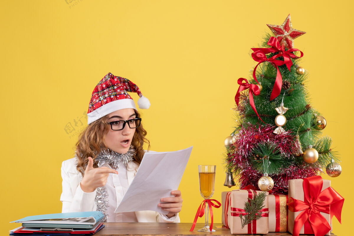 医生前视图女医生坐在圣诞树上 拿着黄色背景上的文件背景成人情感