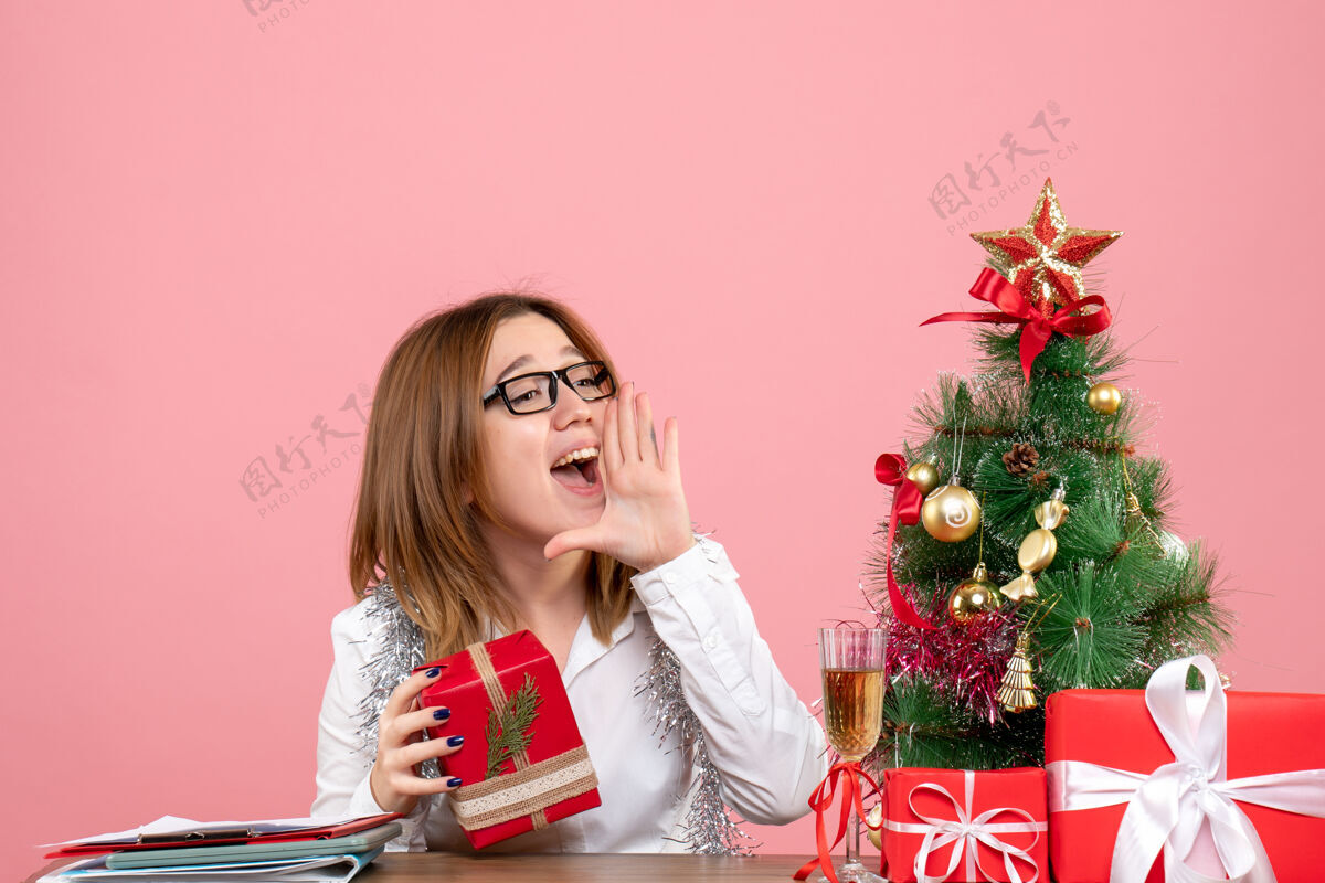 粉红色女工人坐在粉红色的圣诞礼物和圣诞树旁的正视图办公室肖像女工人