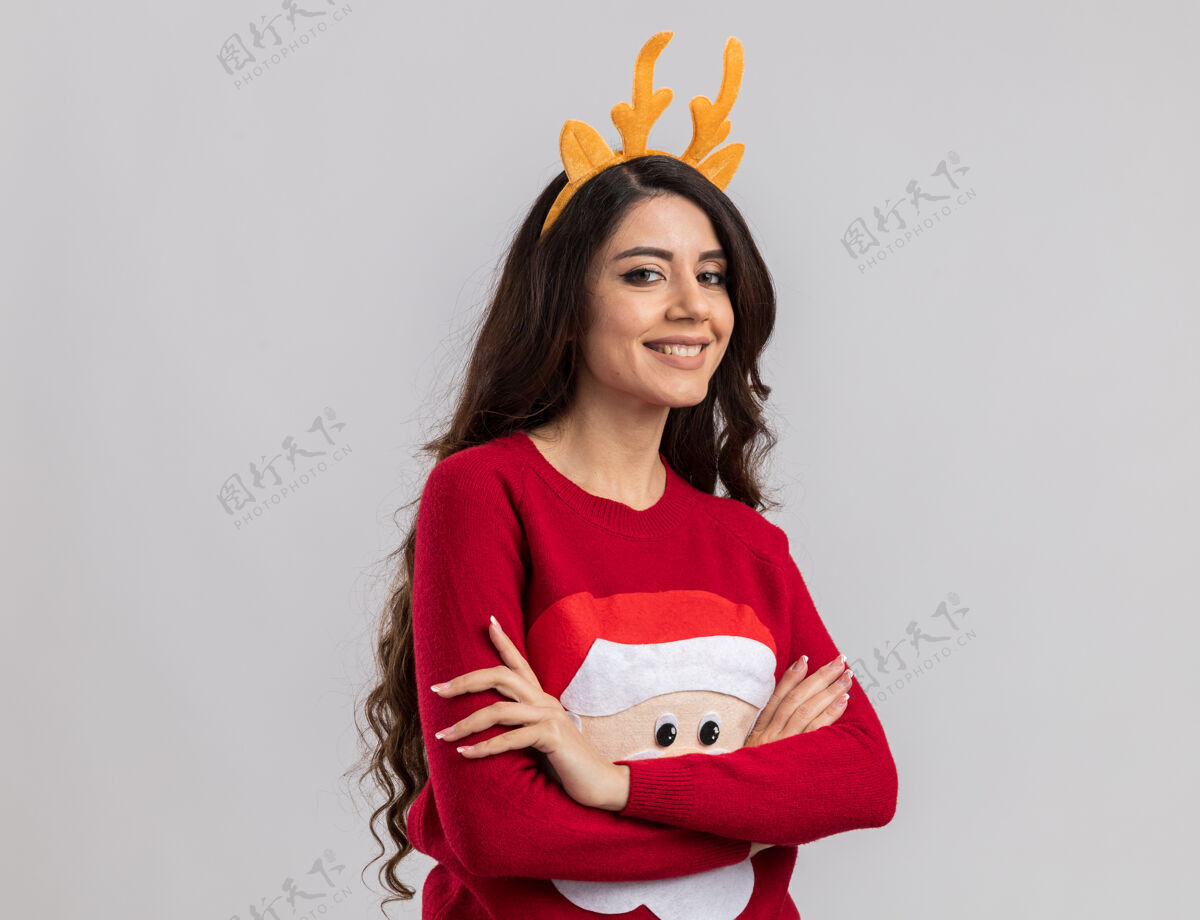 年轻带着驯鹿鹿角头带和圣诞老人毛衣微笑的年轻漂亮女孩站着女孩圣诞快乐