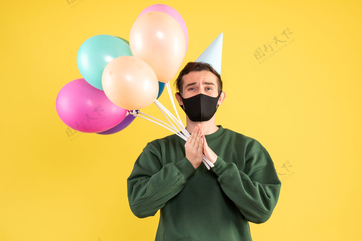 男人正面图：戴着派对帽 站在黄色地面上的彩色气球的年轻人气球人聚会