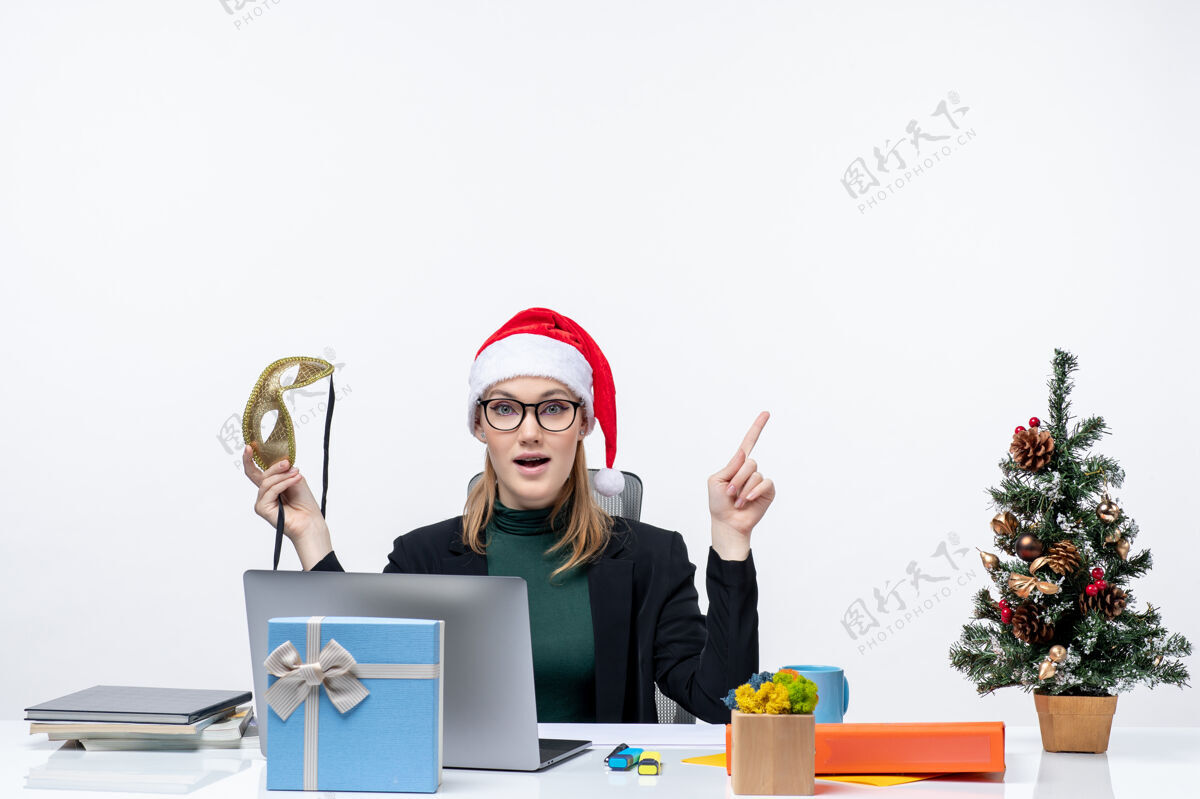 圣诞老人一个戴着圣诞老人帽子戴着眼镜的漂亮女人坐在桌子旁 手里拿着圣诞礼物 坐在办公室里眼镜笔记本电脑桌子