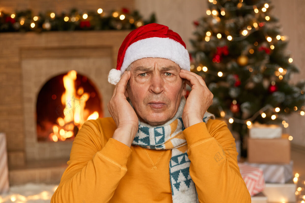 水平戴着圣诞帽的老男人看着相机 手放在太阳穴上沮丧压力老年人
