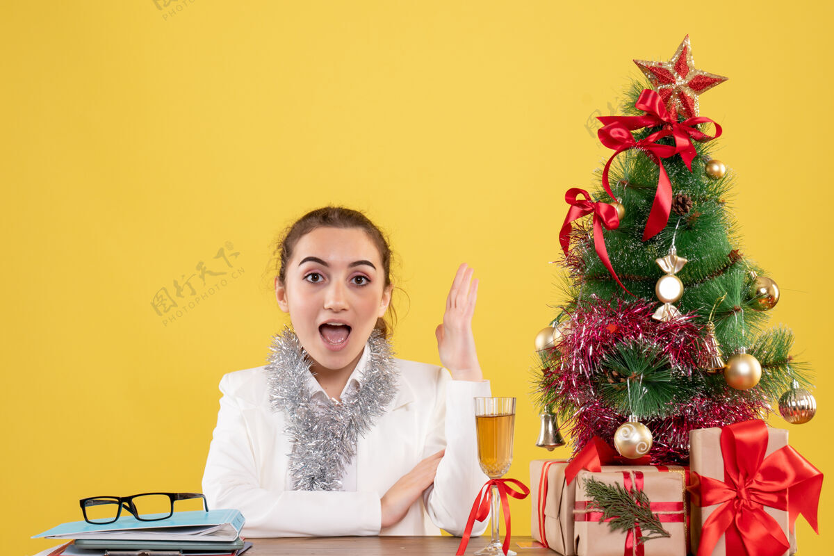 情感正面图女医生围坐在黄色背景上的圣诞礼物和圣诞树旁微笑插花插花