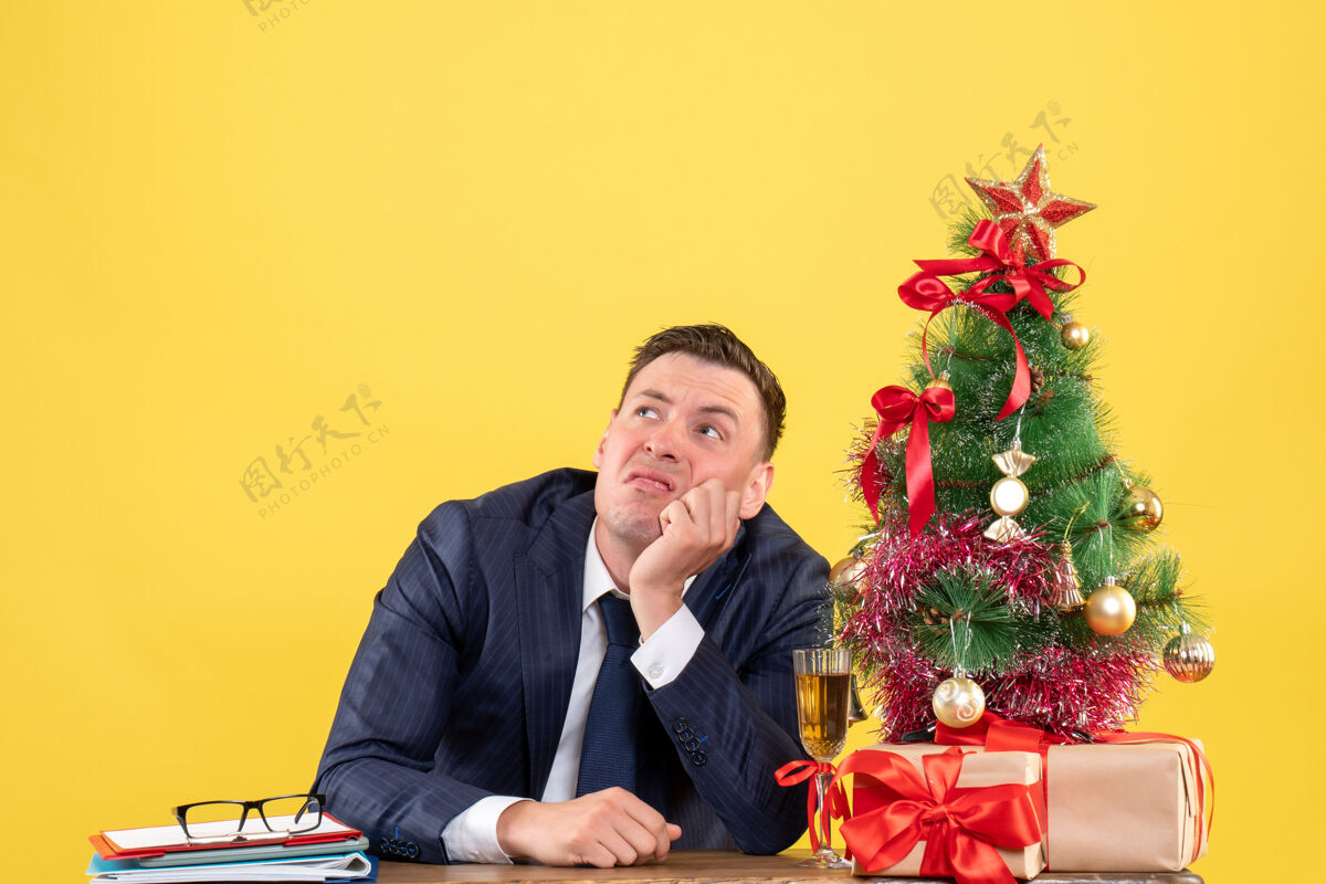 体贴的男人体贴的男人看在圣诞树和黄色礼物旁边的桌子旁高高的标志的前视图办公室桌子商人